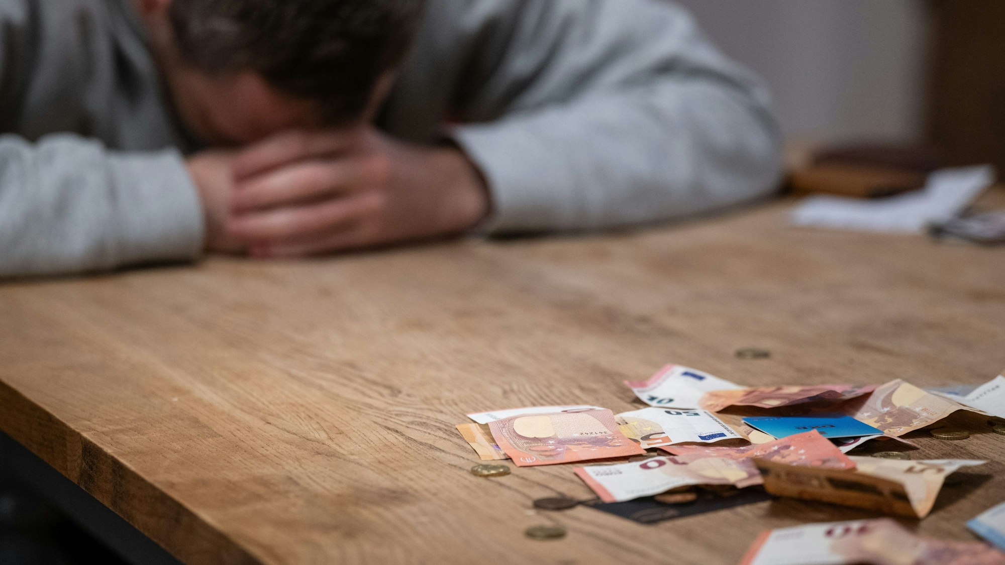 Ein Mann hat seinen Kopf auf seine Hände gelegt, während sich vor ihm Geldscheine, Münzen und Bankkarten auf einem Tisch befinden. (Symbolbild)