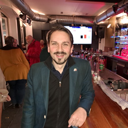 Matthias Großgarten (SPD), ein junger Mann mit dunklem Bart, steht an einer Theke in Niederkassel.