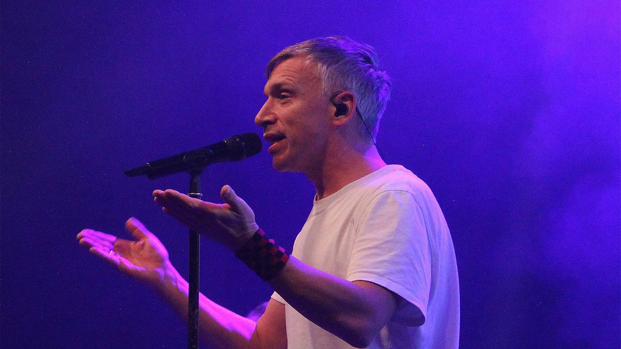 Der Frontman der kölschen Band Kasalla, Bastian Kampmann, steht vor einem Mikrofon und singt.