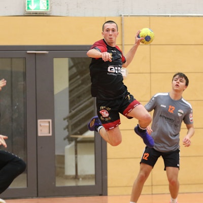 Palmersheims Timo Johnen steigt mit dem Ball in der Hand zum Sprung hoch. Ein Gegenspieler schaut zu, der Torwart hält eine Hand hoch.