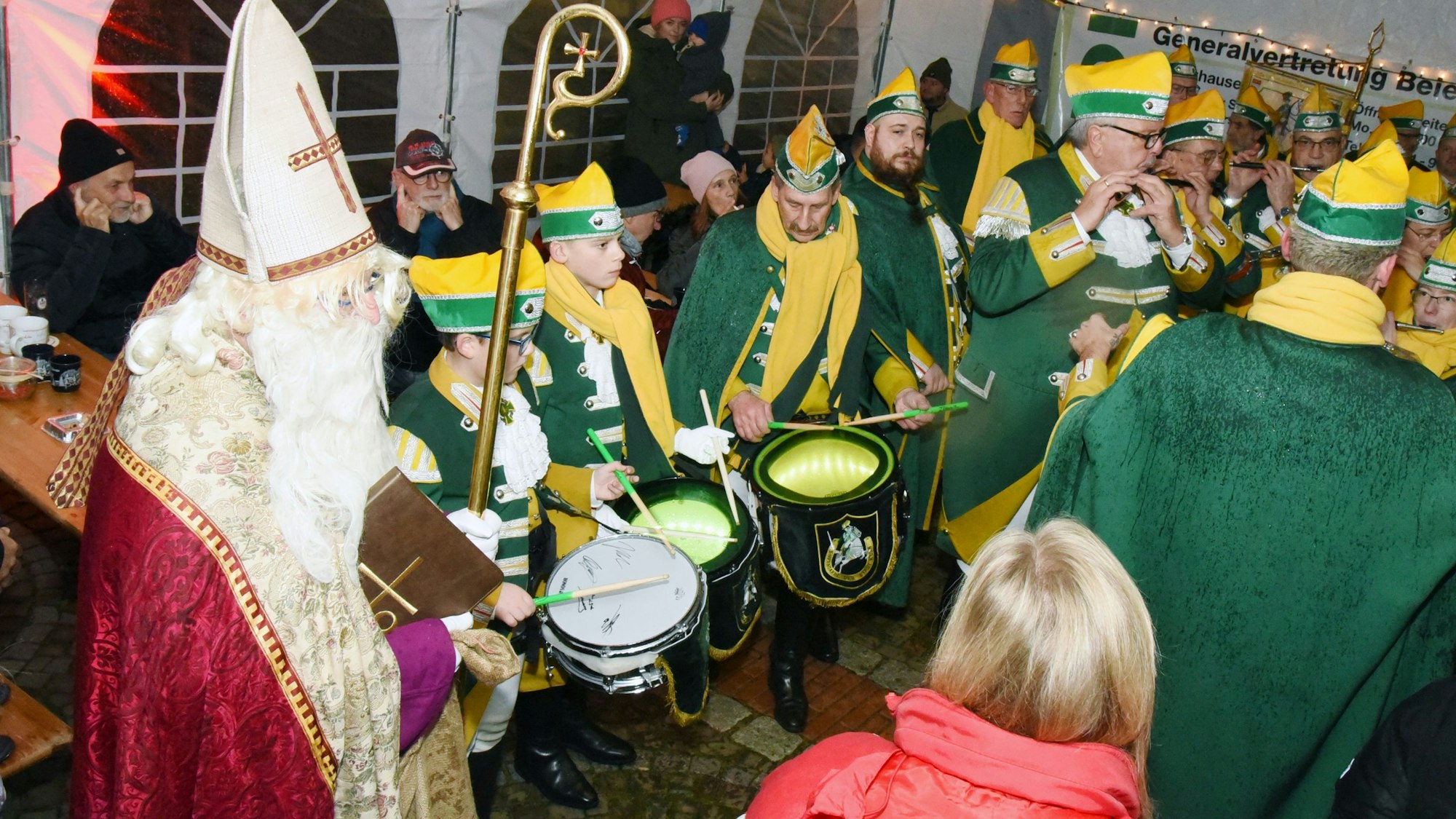 Ein Mann im Nikolaus-Kostüm steht inmitten von Musikern des Spielmannszugs der Ehrengarde in einem weißen Zelt.