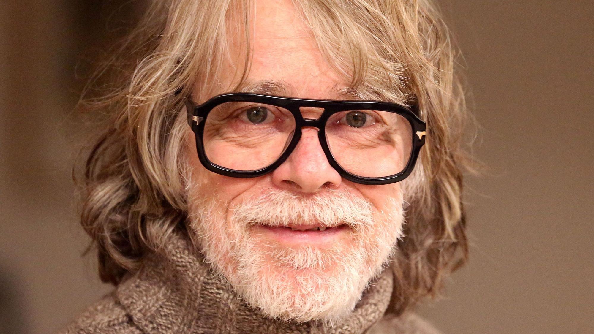 Der Musiker Helge Schneider lächelt in seiner Wohnung.