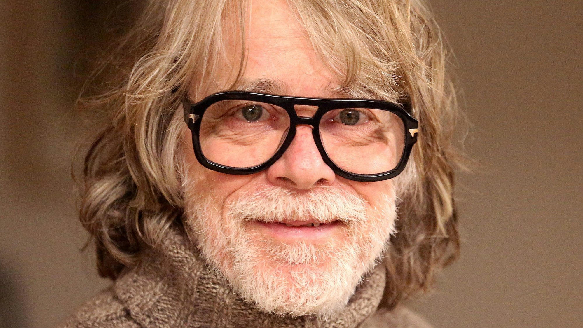 Der Musiker Helge Schneider lächelt in seiner Wohnung.