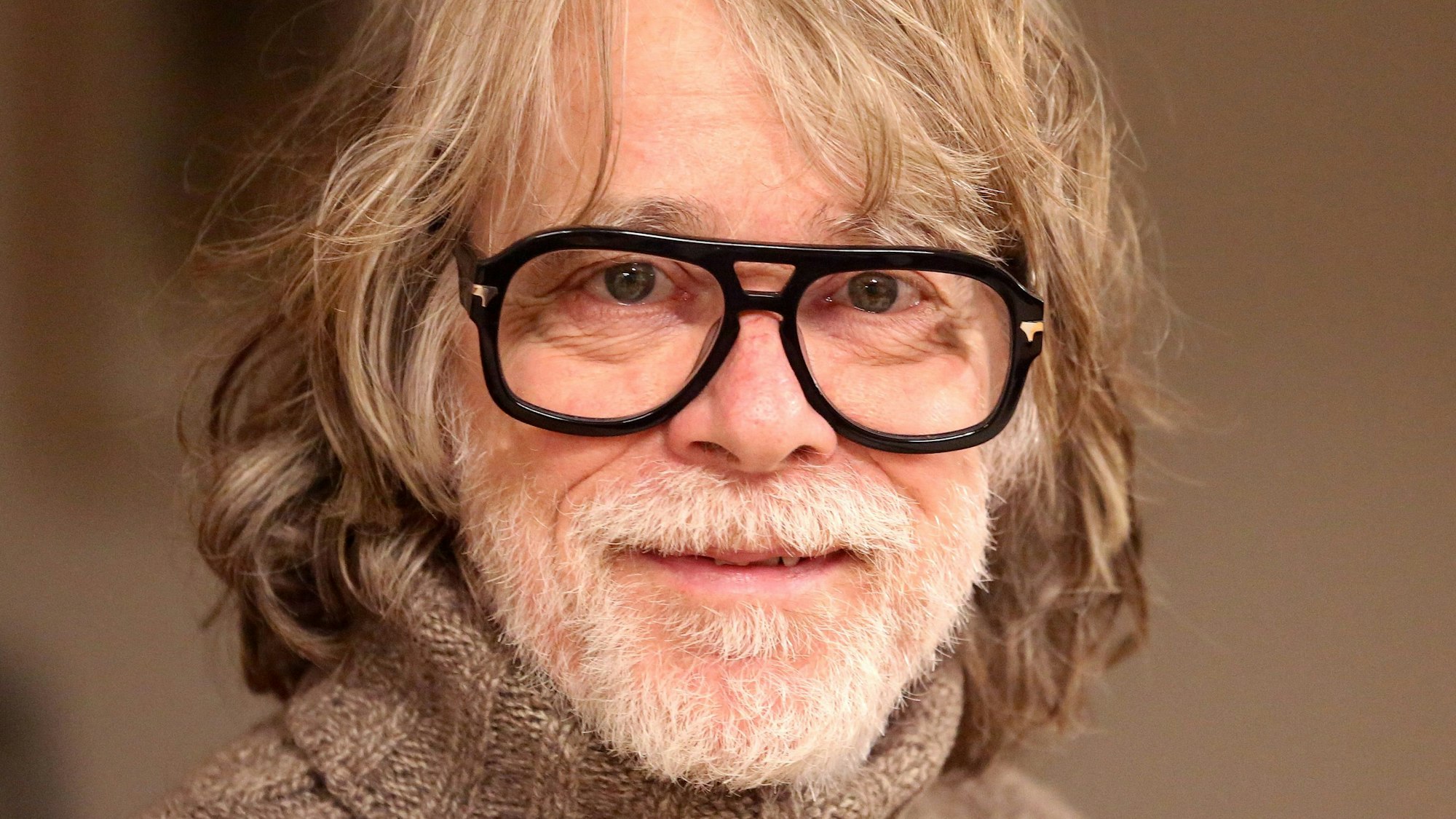 Der Musiker Helge Schneider lächelt in seiner Wohnung.