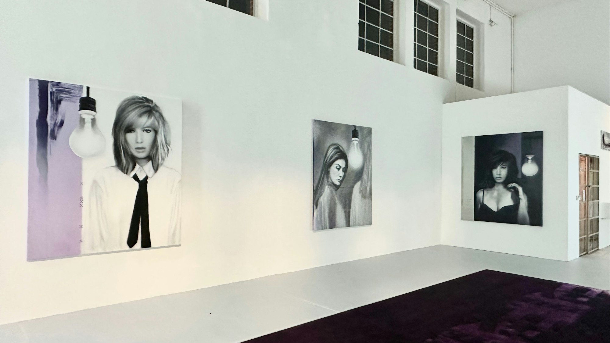 Großformatige Bilder von Frauen hängen an einer weißen Wand.