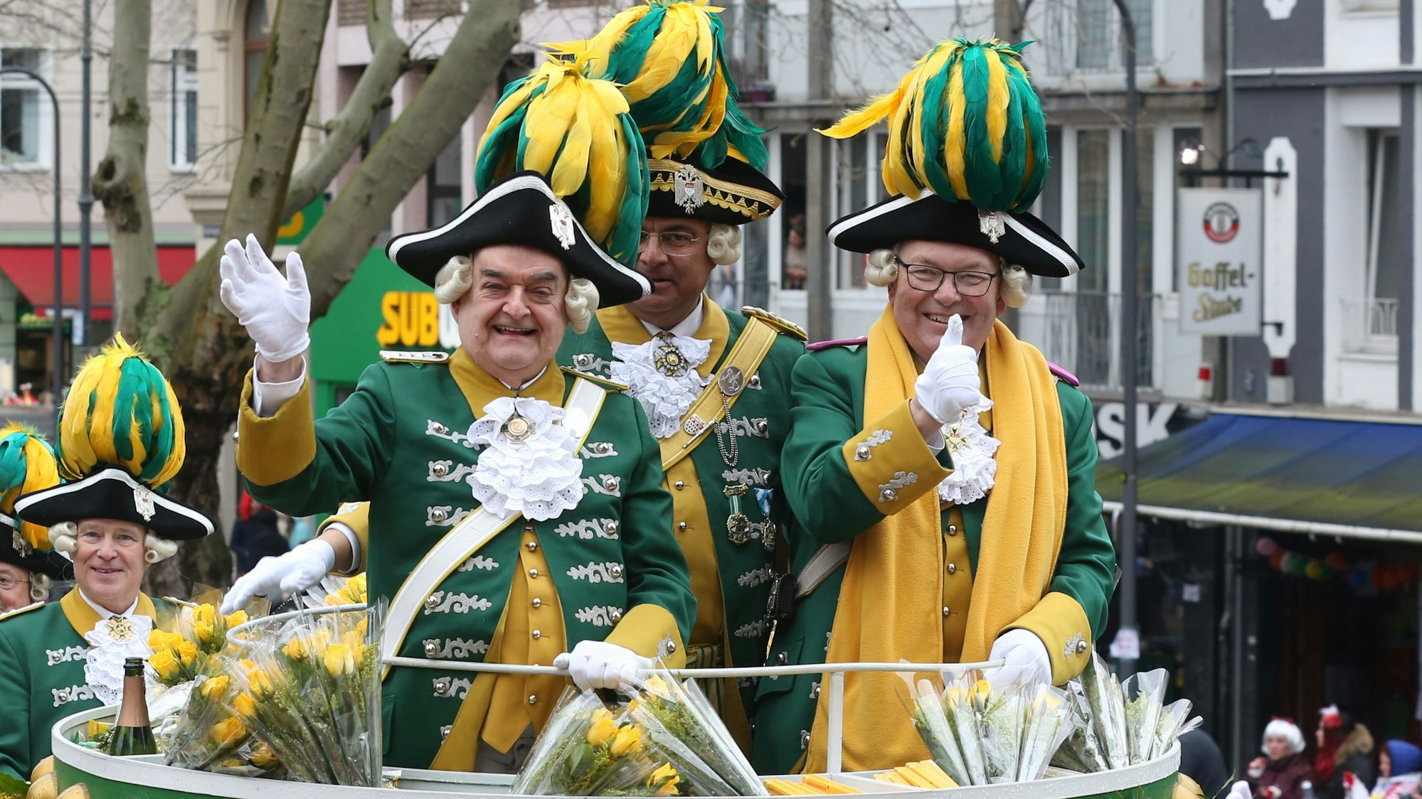 Innenminister Herbert Reul ist in einer historischen gelb-grünen Uniform auf einem Rosenmontagswagen zu sehen. Er winkt lached in die Menge.