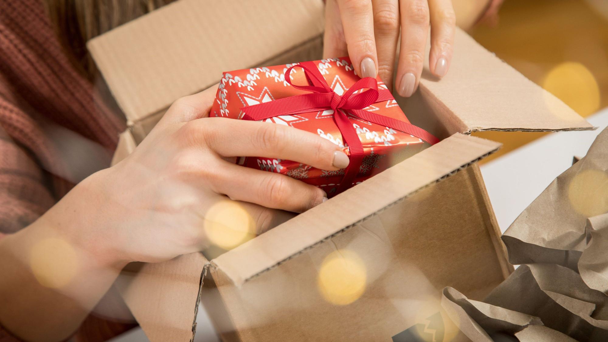 Eine Person legt ein kleines Weihnachtsgeschenk in einen Karton.