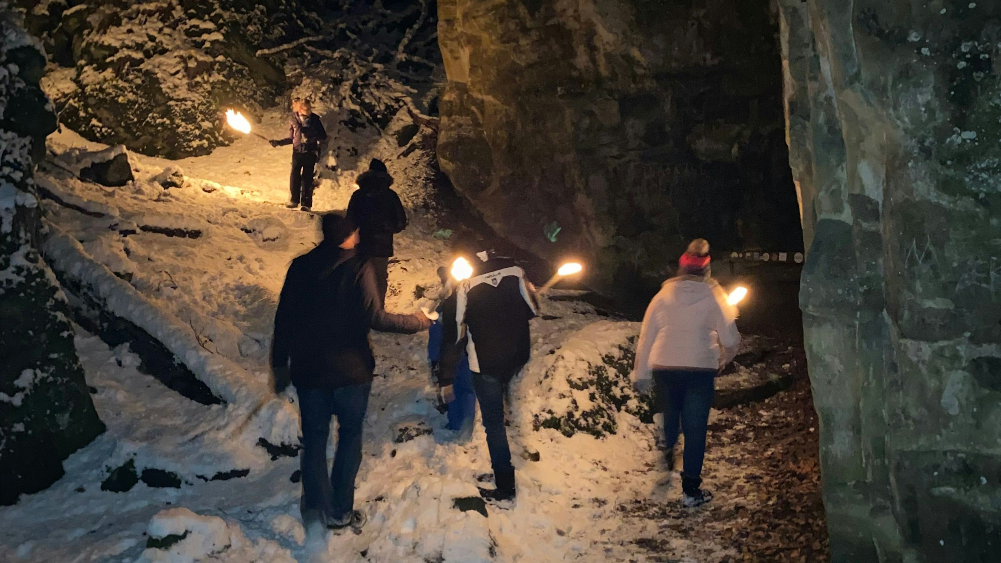 eine Wandergruppe läuft mit Fackeln durch den Schnee an hohen Felswänden vorbei