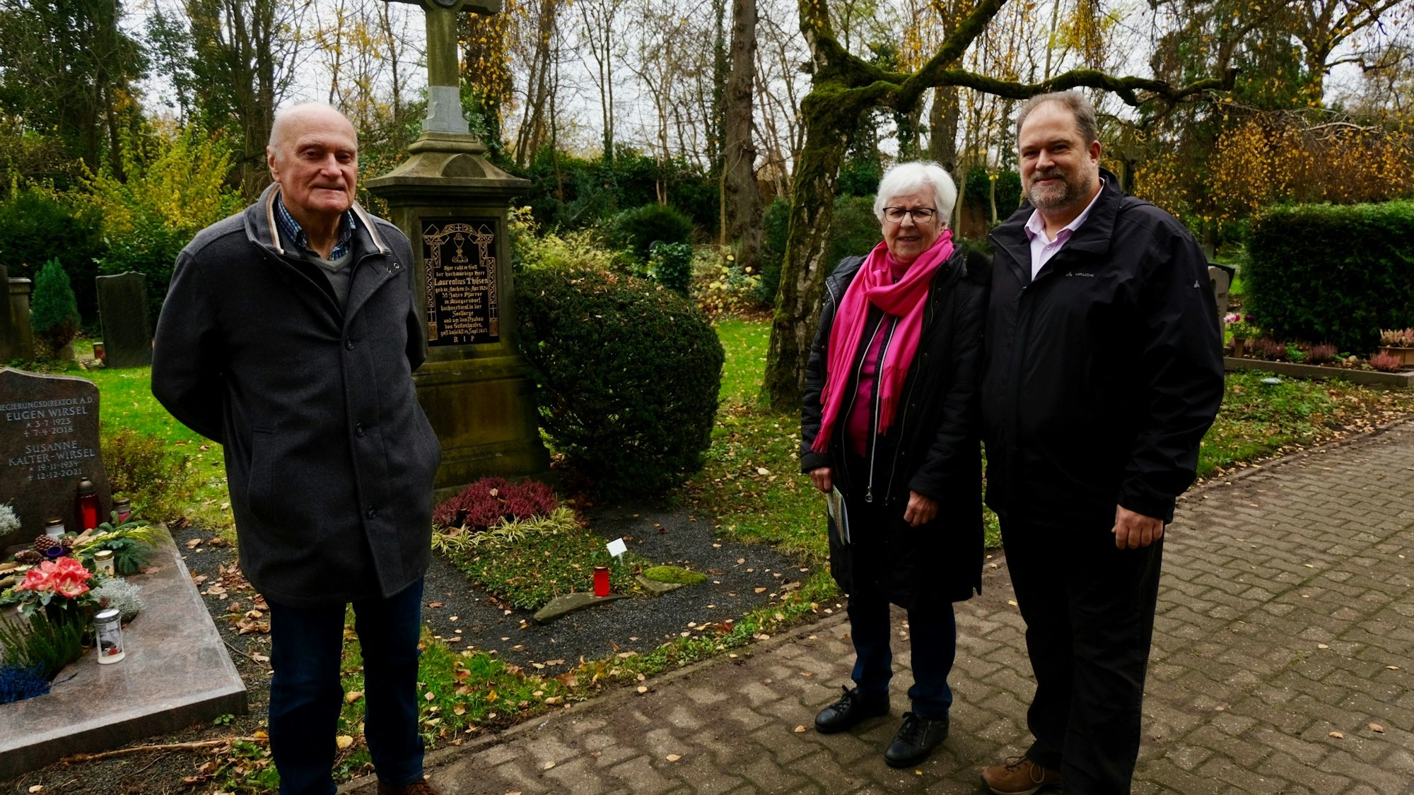 Zwei Männer und eine Frau stehen vor einem Grab.