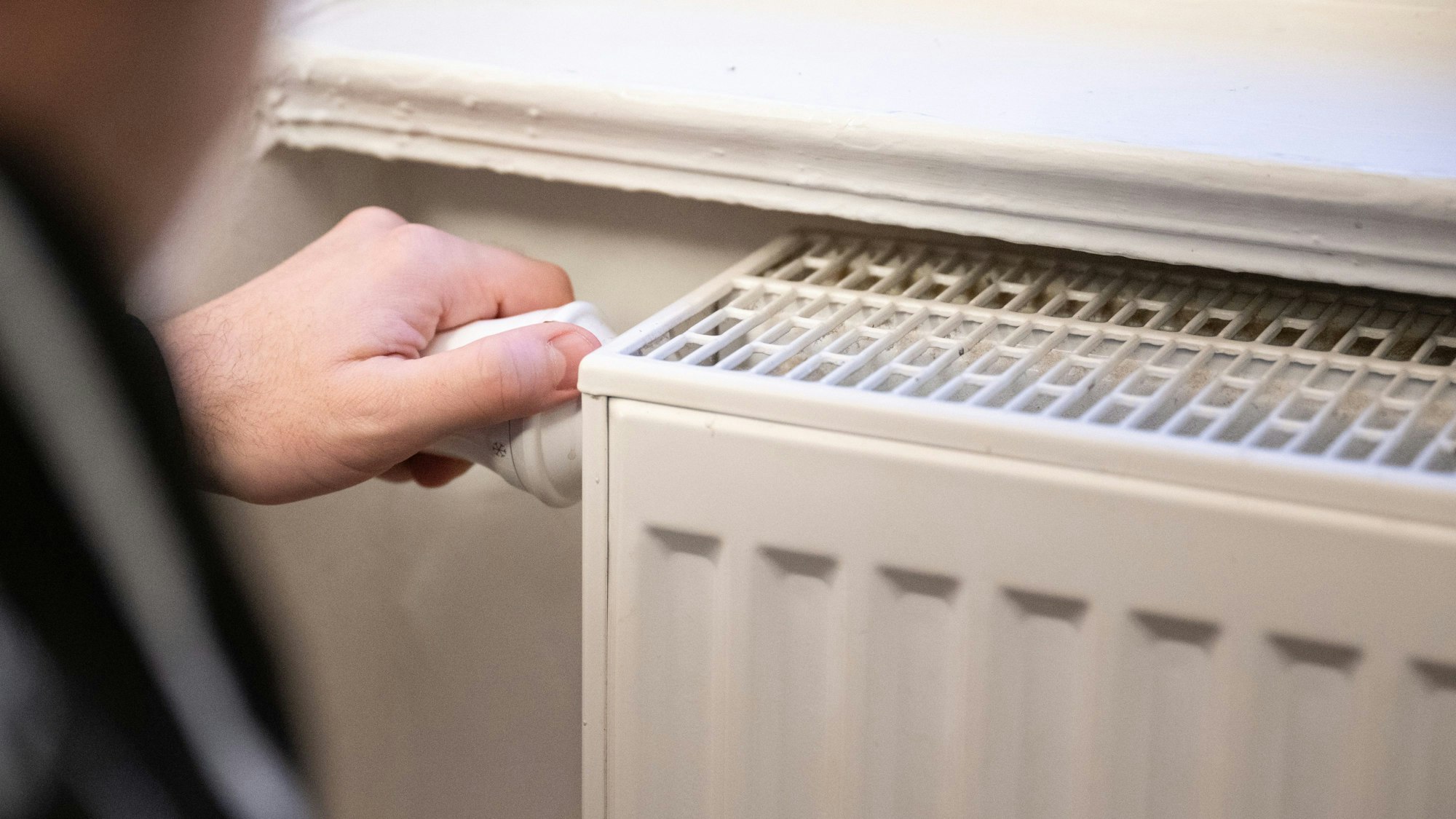 Ein Mann dreht am Thermostat einer Heizung.