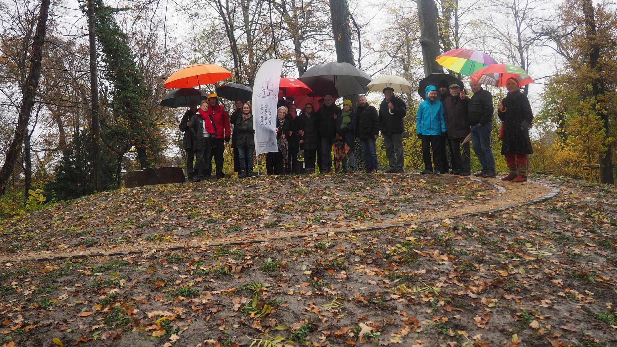 Eine Gruppe Menschen steht auf einem Hügel, auf den ein spiralförmig gewundener Weg führt.