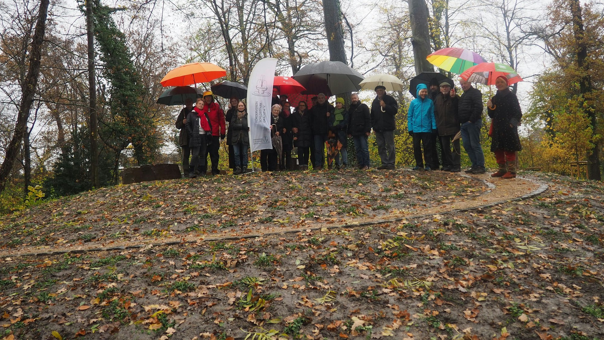 Eine Gruppe Menschen steht auf einem Hügel, auf den ein spiralförmig gewundener Weg führt.