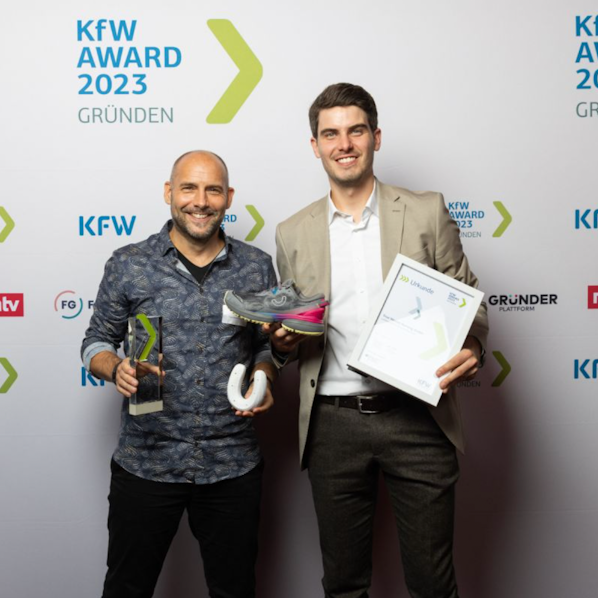 Zwei Männer mit einem Preis, einem Hufeisen, einem Turnschuh und einer Urkunde in der Hand