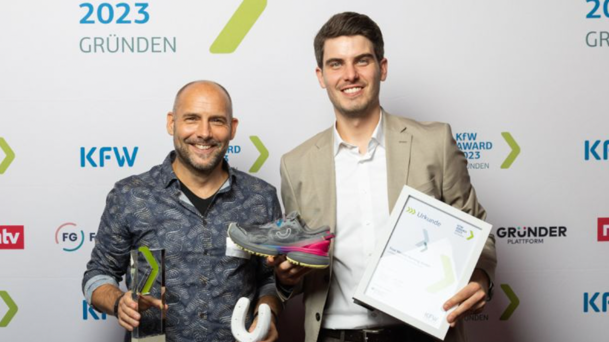 Zwei Männer mit einem Preis, einem Hufeisen, einem Turnschuh und einer Urkunde in der Hand
