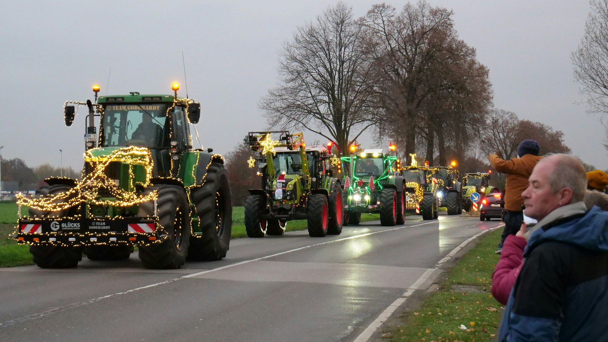 Auf dem Foto sind beleuchtete und geschmückte Traktoren zu sehen. Am Straßenrand stehen Zuschauer.
