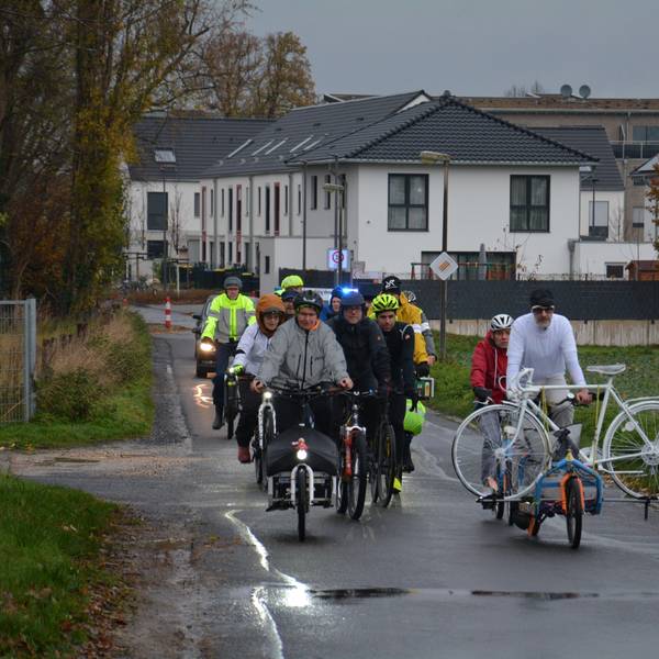 Fahrräder fahren über einen Feldweg, einer transportiert ein weißes Geisterfahrrad.