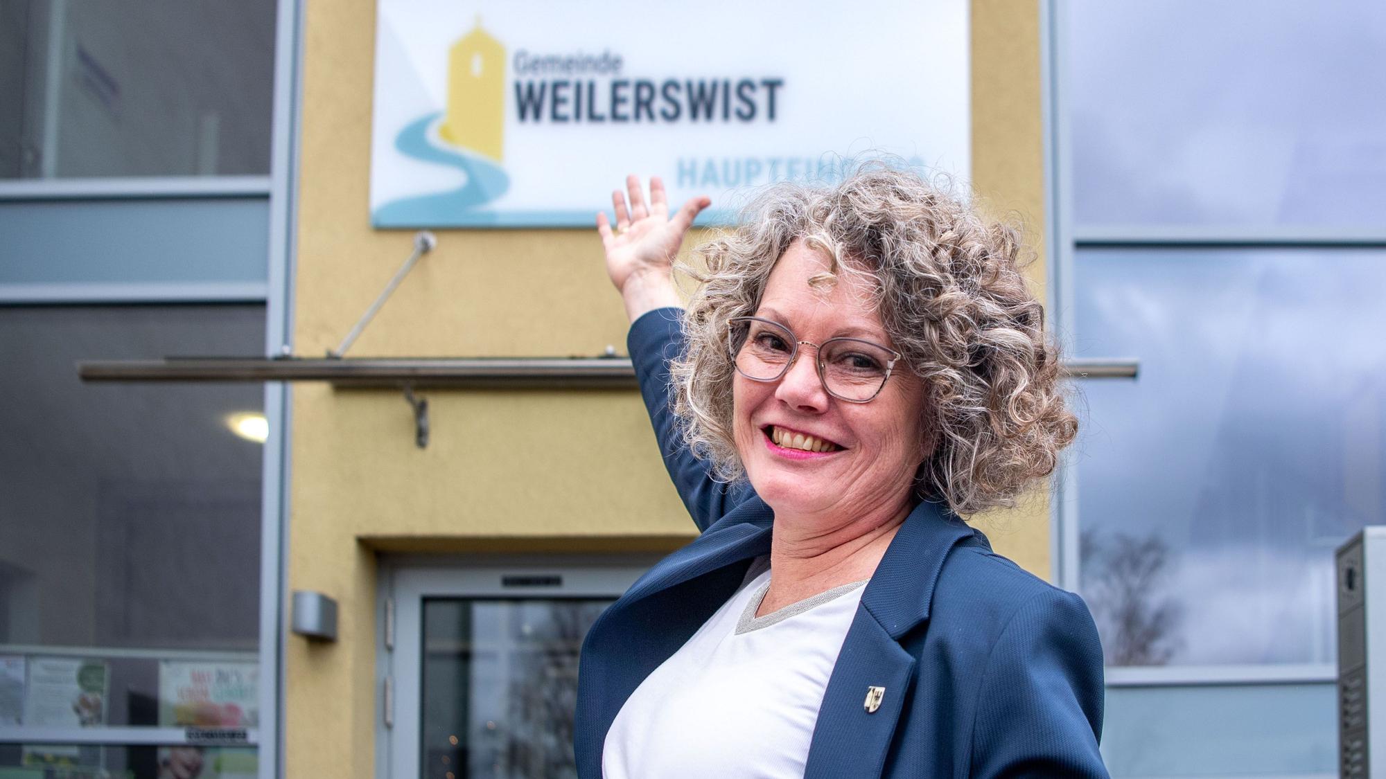 Das Bild zeigt Bürgermeisterin Anne Horst vor dem Rathaus. Sie zeigt auf das Plakat mit dem neuen Logo, das an der Fassade befestigt ist.