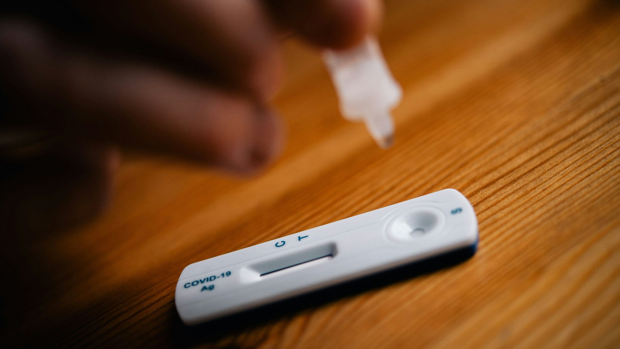 Ein Corona-Schnelltest liegt auf einem Holztisch. Eine Hand hält die kleine Testampulle.