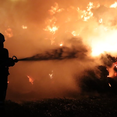 Das Bild zeigt einen Feuerwehrmann, der vor einer Feuerwand steht.