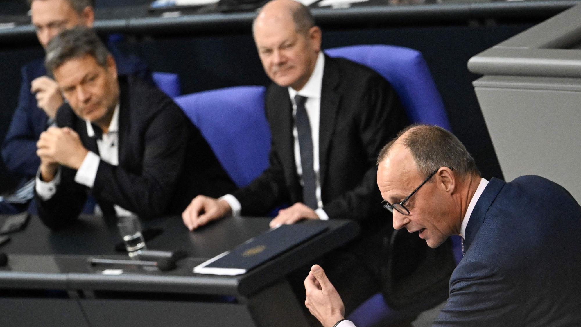 Friedrich Merz (vorne) hält seine Rede im Bundestag, im Hintergrund sind Finanzminister Christian Lindner, Wirtschaftsminister Robert Habeck und Bundeskanzler Olaf Scholz zu sehen (v. l. n. r.).