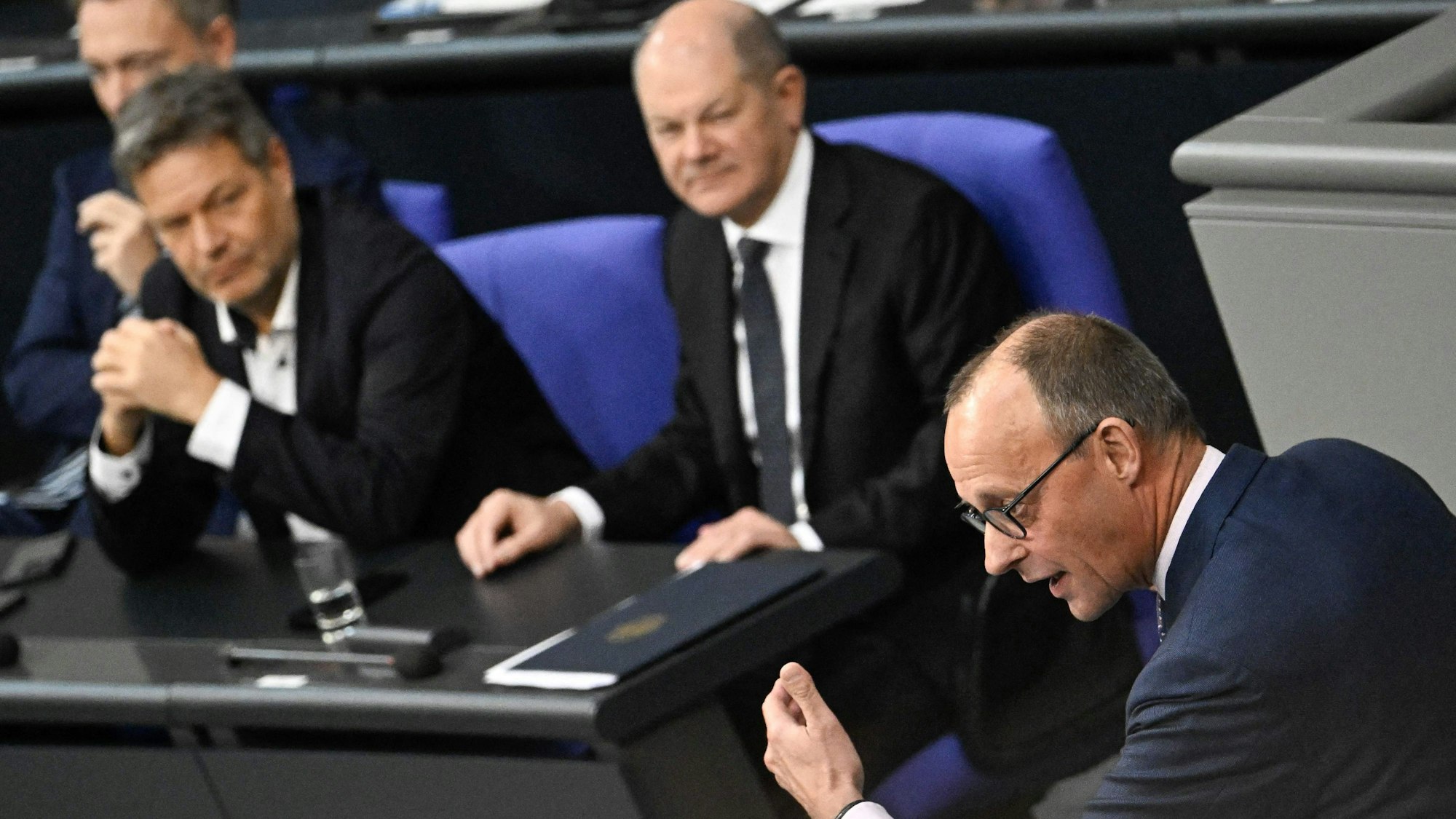 Friedrich Merz (vorne) hält seine Rede im Bundestag, im Hintergrund sind Finanzminister Christian Lindner, Wirtschaftsminister Robert Habeck und Bundeskanzler Olaf Scholz zu sehen (v. l. n. r.).