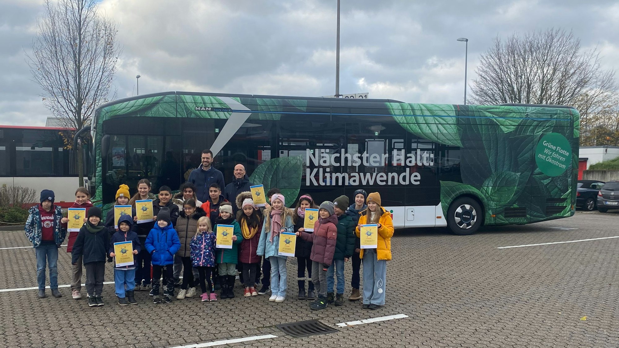 Grundschüler und Kindergartenkinder stehen vor einem Bus auf dem "Nächster Halt: Klimawende" steht. Bei den Kindern stehen Lars Dietrich (Leiter Naturgut Ophoven) und Marc Kretkowski (Geschäftsführer wupsi)