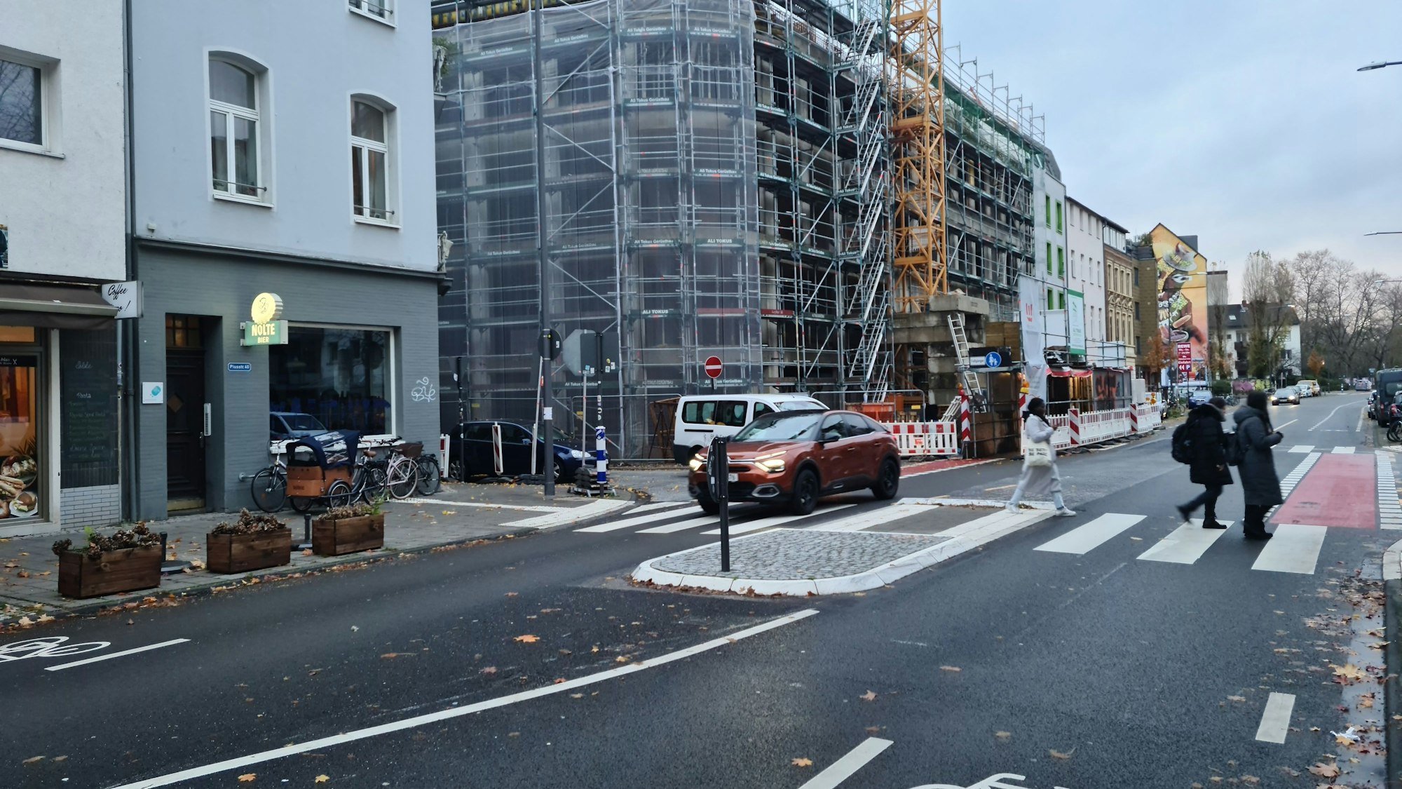 Eine mehrspurige Straße mit Zebrastreifen, Fußgängern und Baustelle ist zu sehen.