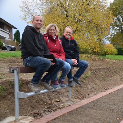 Sie fühlen sich wohl auf der Jugendbank und vor allem auf dem neuen Dorfplatz mitten in Waldbröl-Rossenbach (von links): Landschaftsgärtner und Chefplaner Tobias Pinger sowie Katja Grunewald und Georg Brenner vom Vorstand des Dorfvereins. Die Drei sitzen auf einer der neuen Jugendbänke an dem Platz.