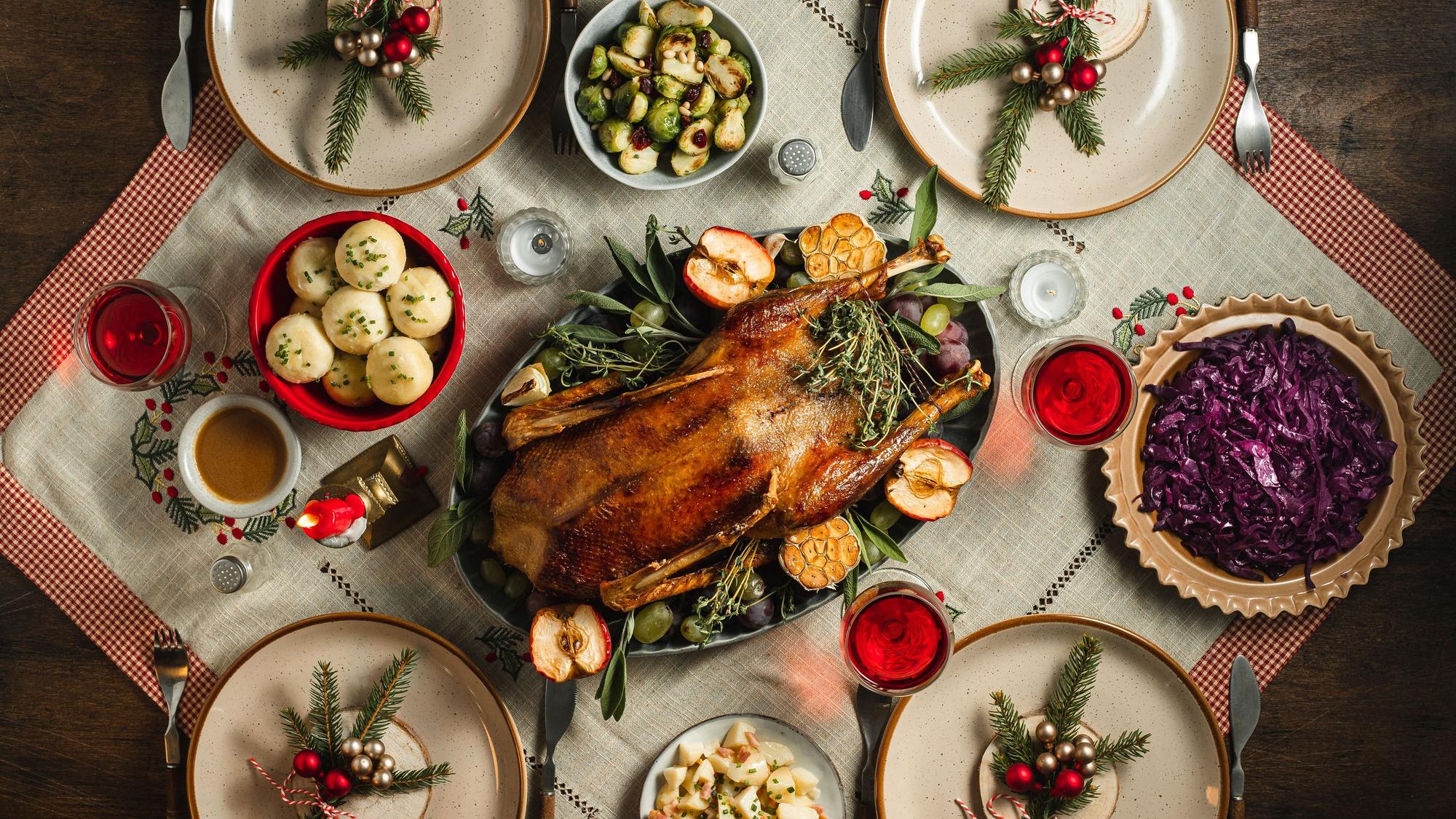 Symbolbild: Ein traditionelles deutsches Weihnachtsessen mit Gans, Rotkohl und Klößen auf einem festlich gedeckten Tisch.