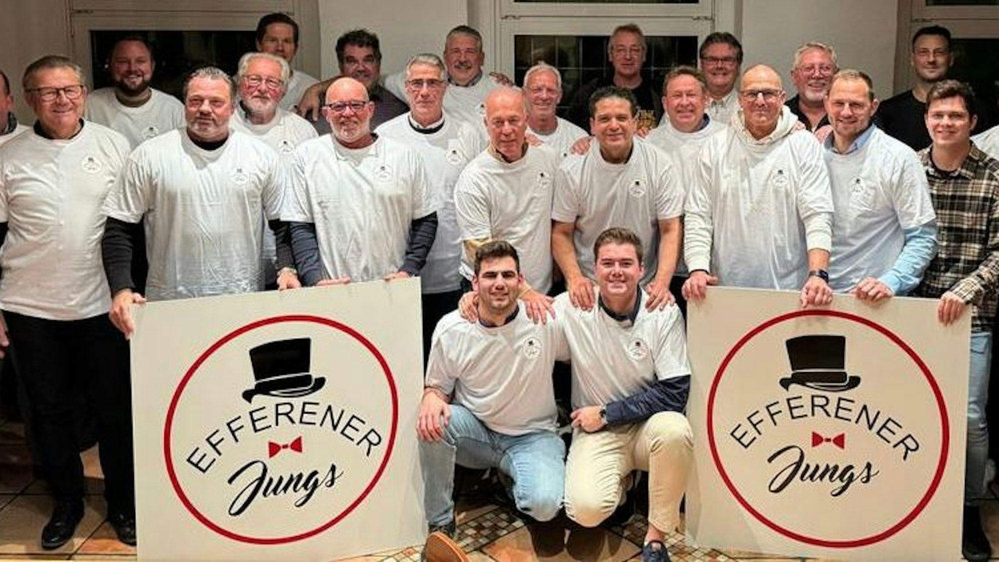 Das Foto zeigt eine Gruppe von Männern in weißen T-Shirts mit zwei großen Schildern mit dem Vereinslogo.