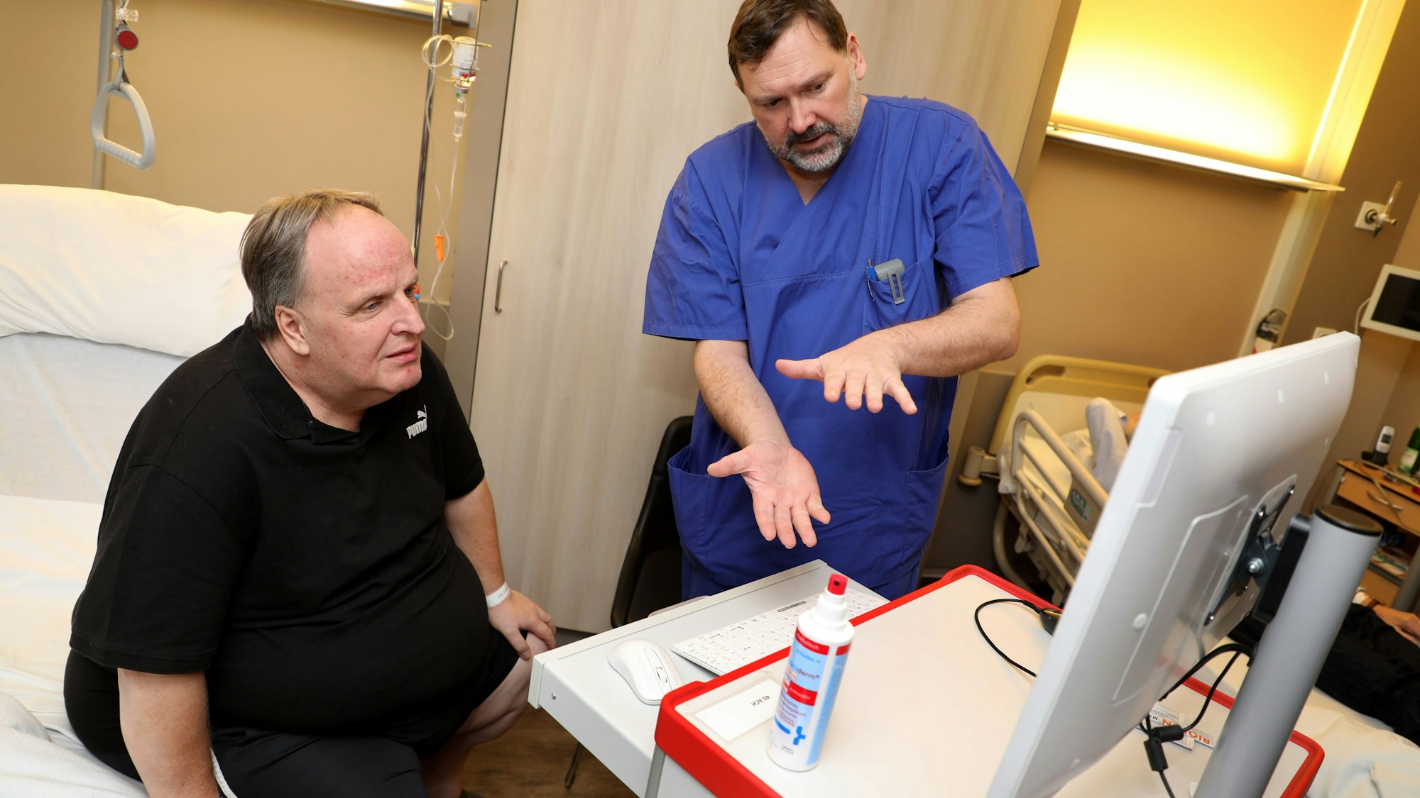 Ein Mediziner erklärt einem Patienten etwas an einem Bildschirm.