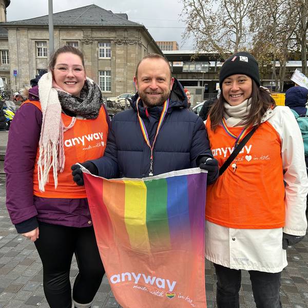 Ein Mann und zwei Frauen mit einer Regenbogenfahne