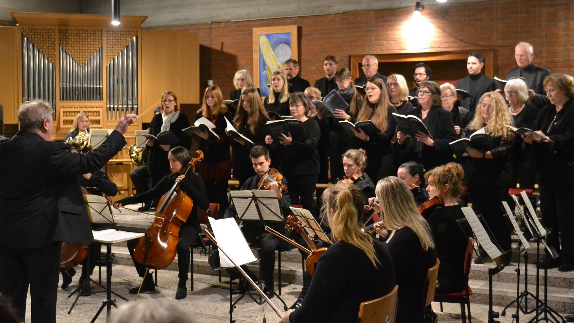 Ein Chor singt in schwarzer Kleidung, davor sitzt ein keines Orchester.