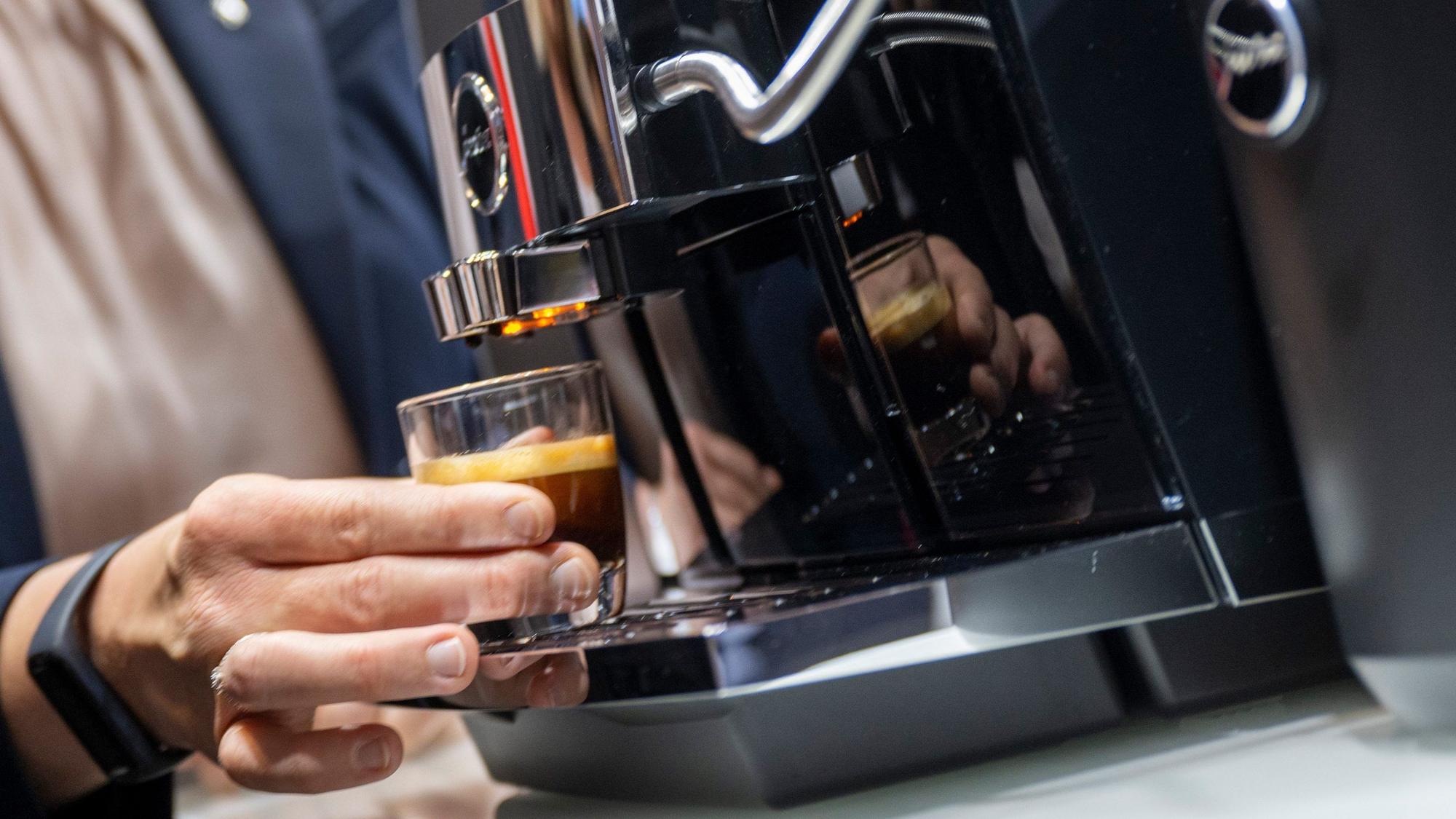 Eine Hand hält einen frisch gebrühten Espresso an einem Kaffeevollautomaten.
