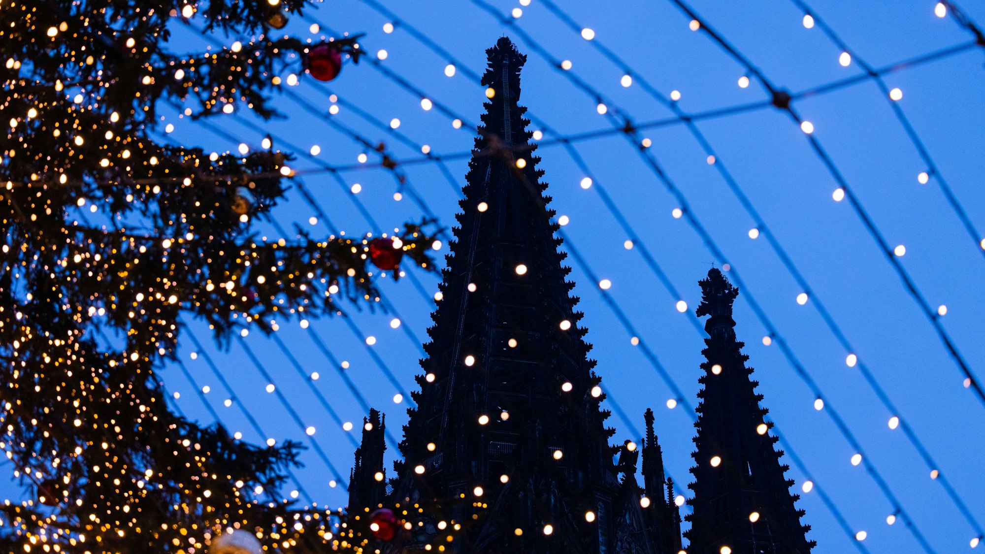 Spitzen des Kölner Doms sind hinter der Beleuchtung des Weihnachtsmarkts auf dem Roncalliplatz zu sehen