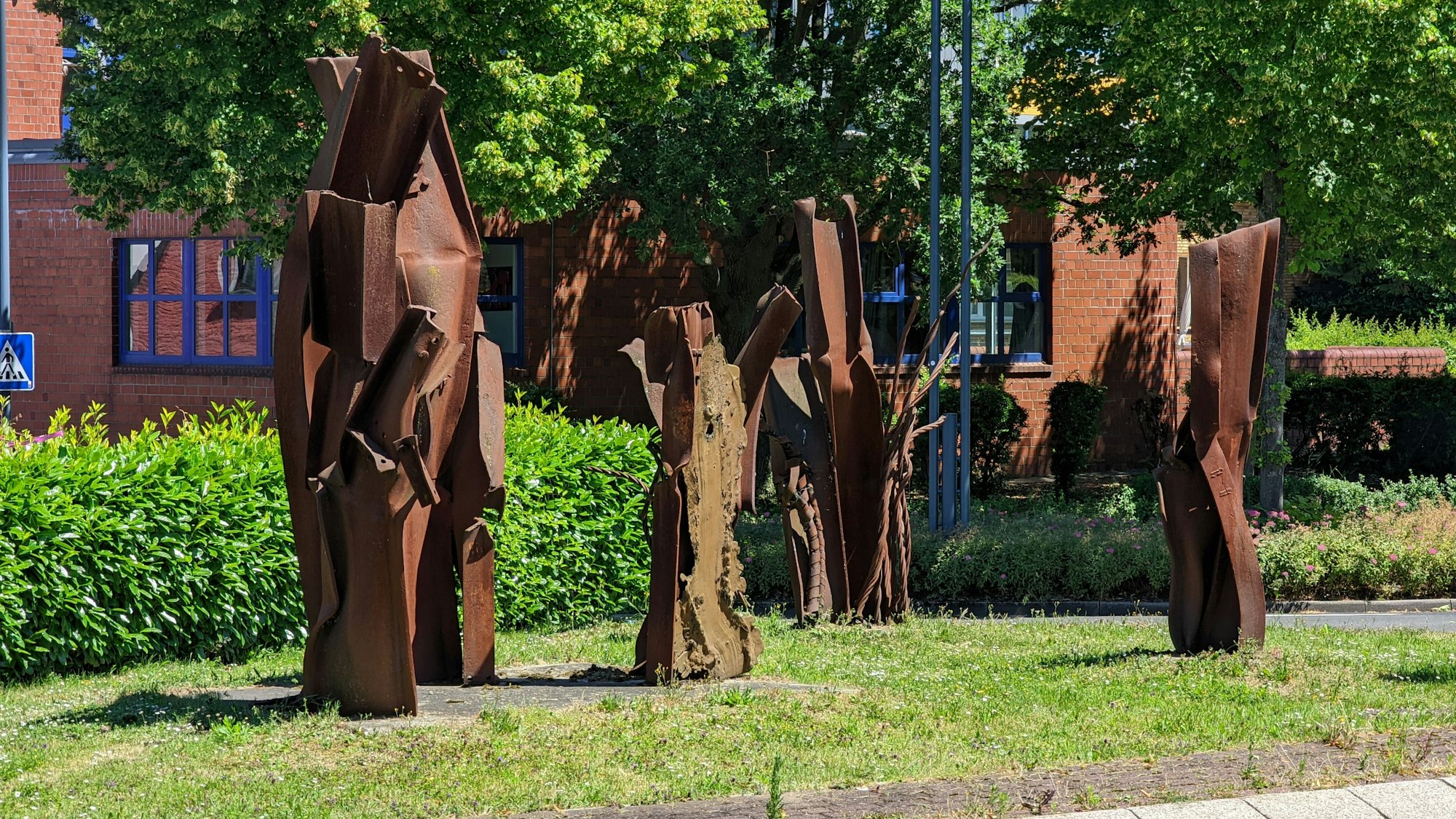 Das Innere eines Kreisverkehrsplatzes in Hermülheim mit Rasen, Hecke und Stahlskulpturen.
