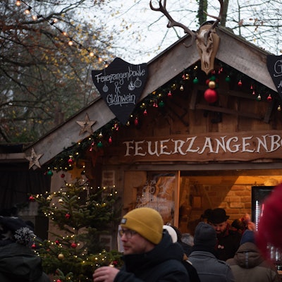 An einer mit roten, grünen und goldenen Weihnachtskugeln geschmückten Holzbude steht „Feuerzangenbowle“.