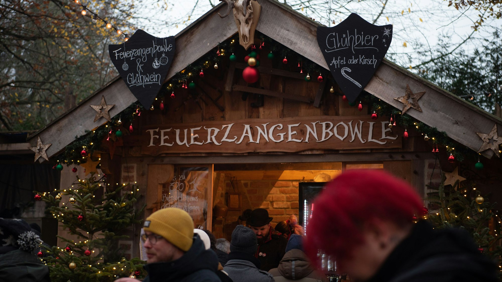 An einer mit roten, grünen und goldenen Weihnachtskugeln geschmückten Holzbude steht „Feuerzangenbowle“.