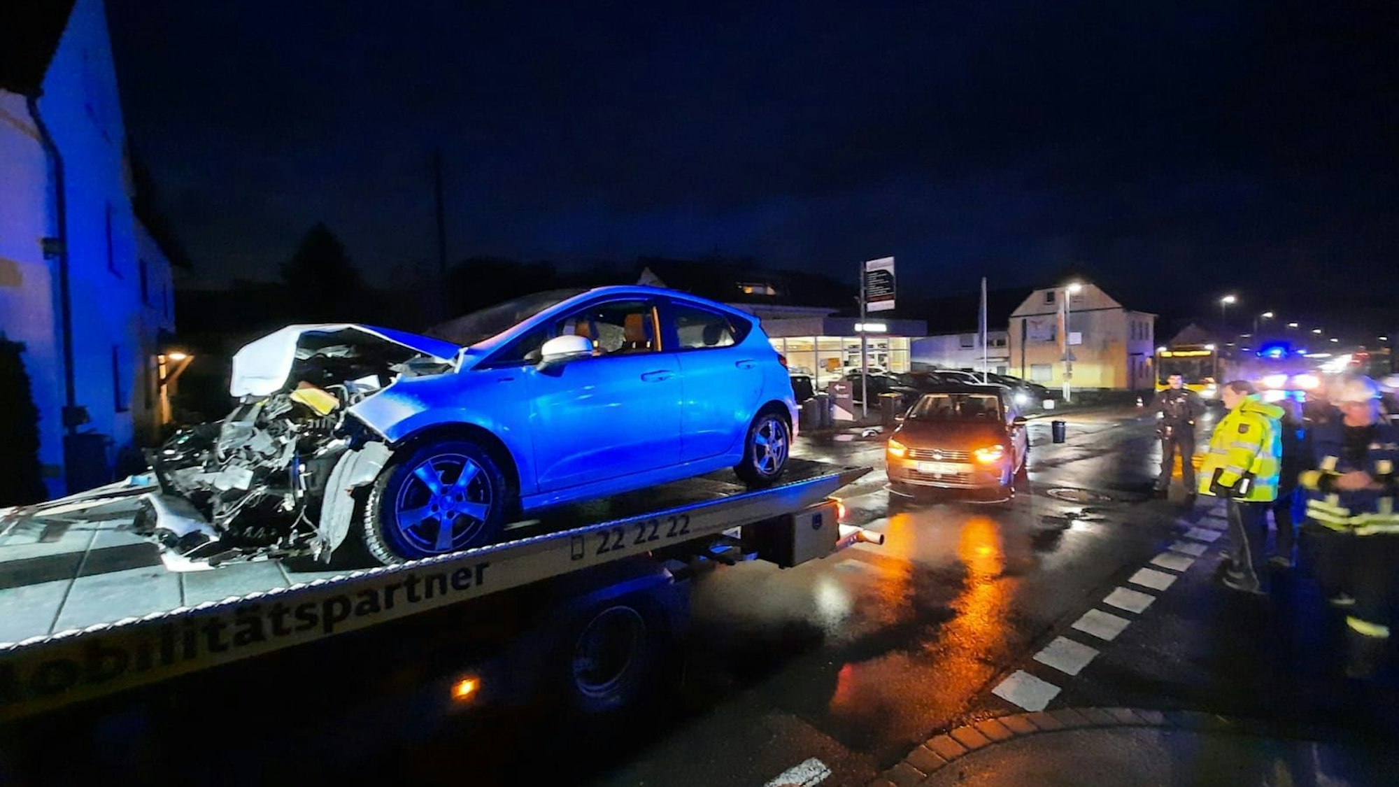 Ein an der Front schwer beschädigter Pkw steht auf einem Abschleppwagen, Polizisten sichern die Unfallstelle ab.