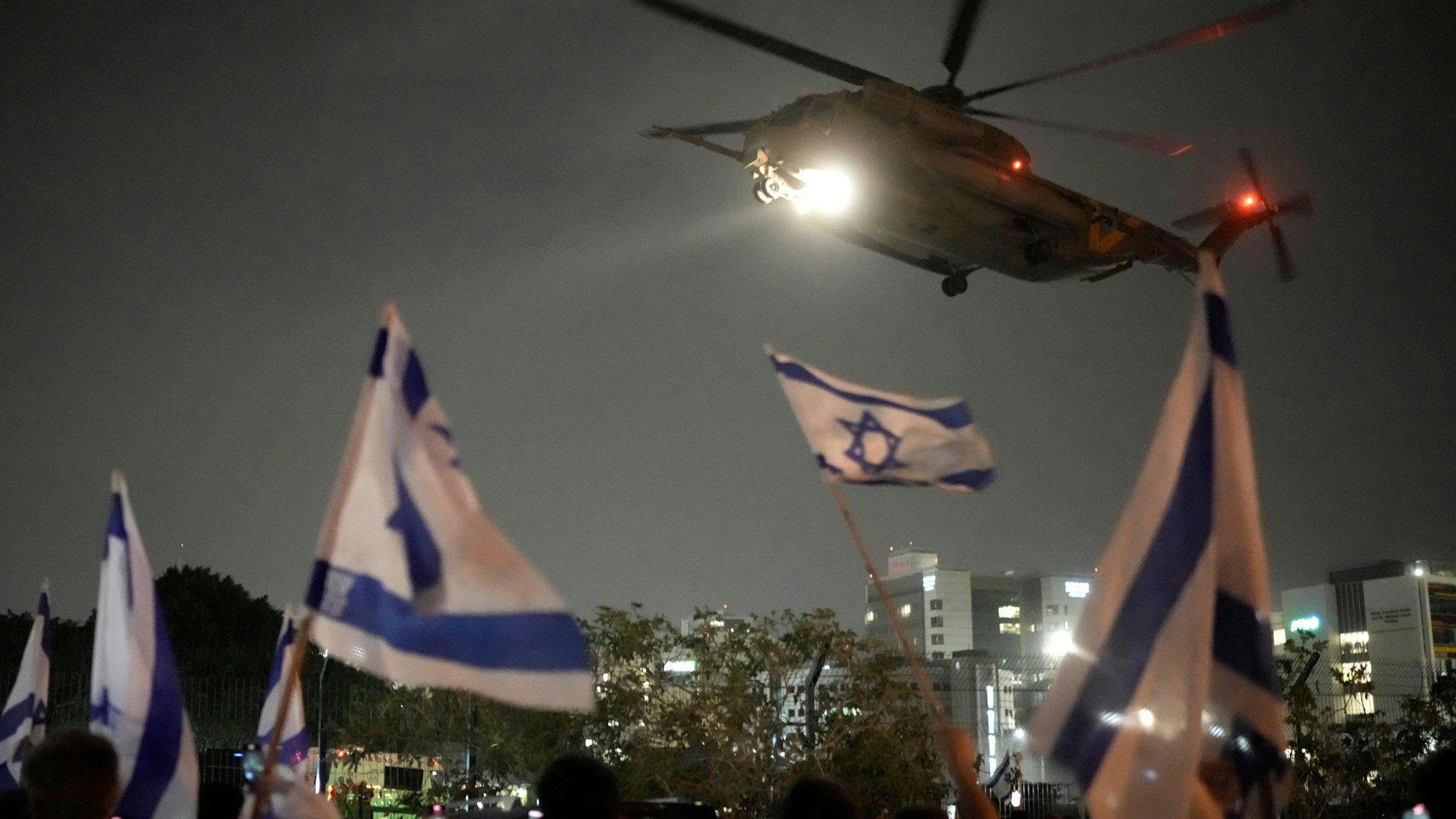 Menschen schwenken israelische Fahnen, während ein Hubschrauber mit Geiseln, die von der Hamas aus dem Gazastreifen frei gelassen wurden, auf dem Hubschrauberlandeplatz des Schneider Children's Medical Center landet.