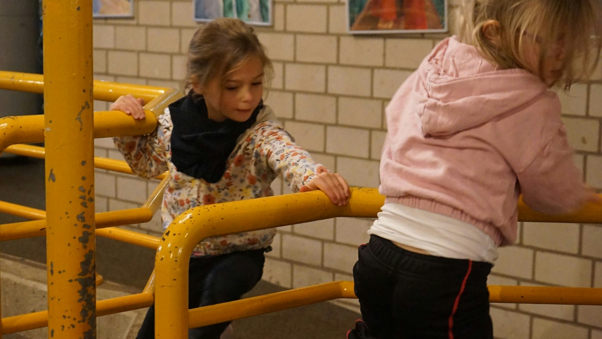 Zwei Mädchen klettern an einem gelben Geländer entlang.