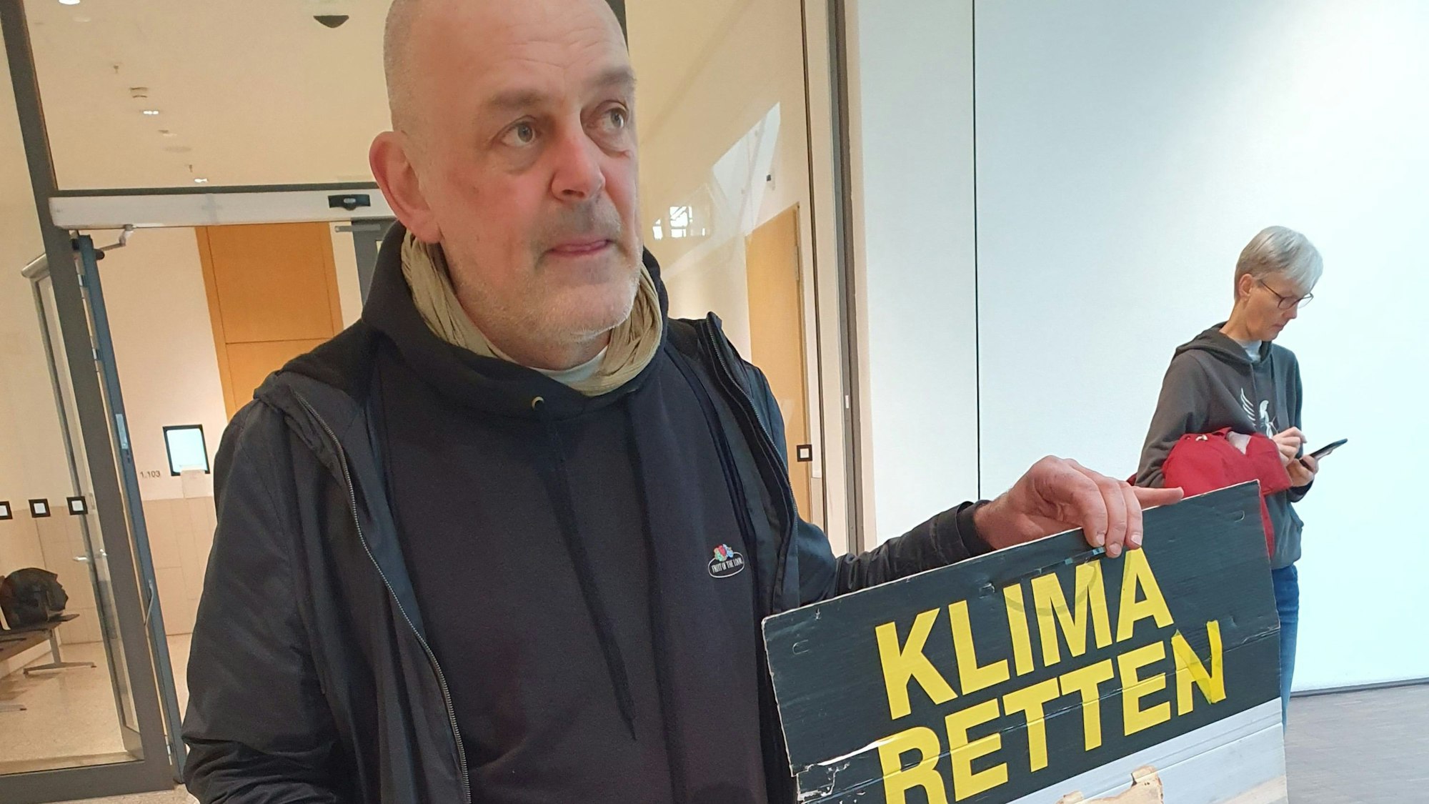 Winfried Bernhardt, Klimaaktivist, steht mit einem Plakat mit der Aufschrift «Klima retten» im Foyer des Gerichts. Wegen einer Attacke mit Kartoffelbrei im NRW-Landtag musste er sich vor Gericht verantworten. Die Staatsanwaltschaft warf ihm Sachbeschädigung vor.
