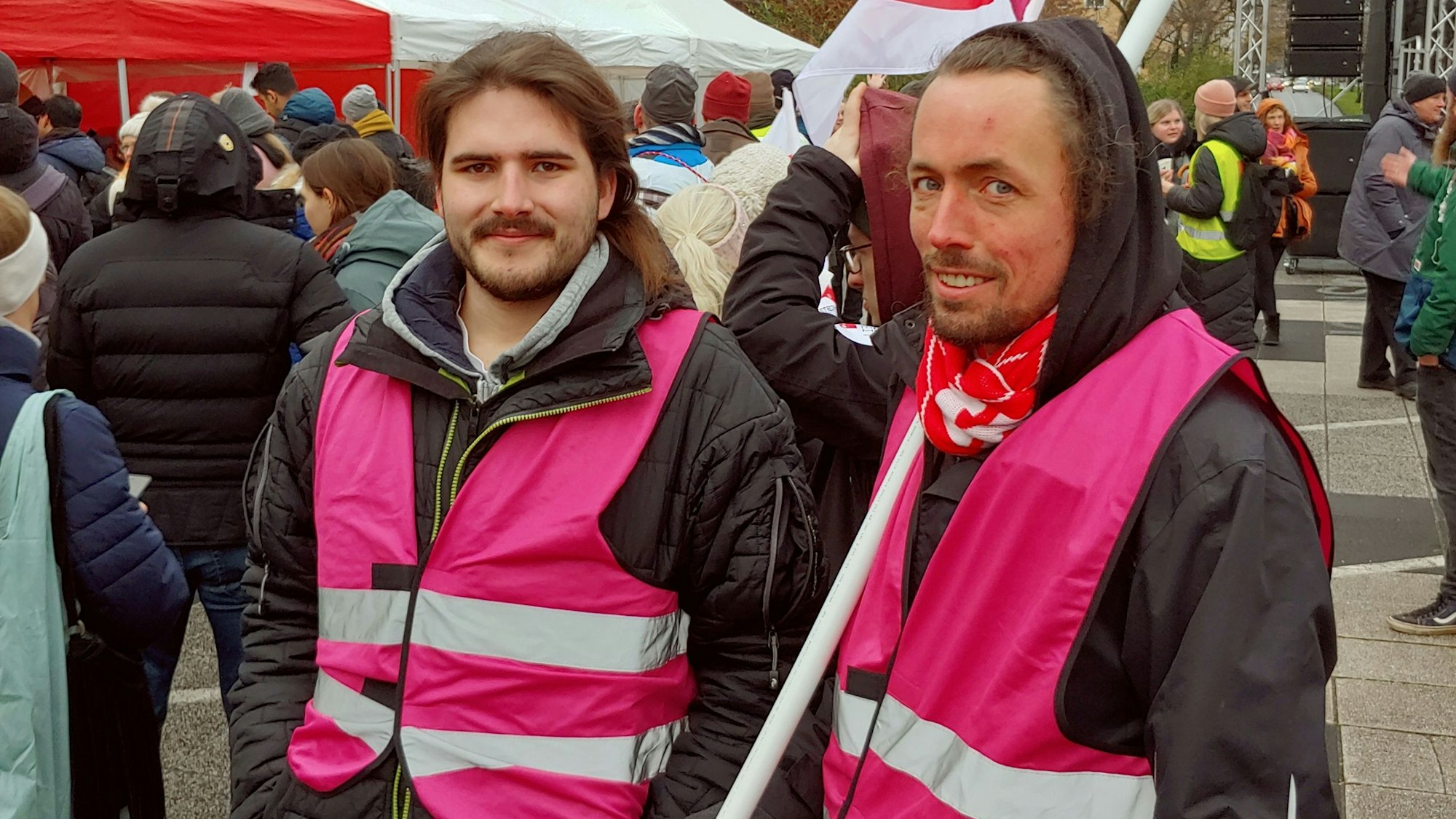 Zwei Junge Männer tragen lilafarbene Warnwesten.