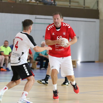 Zülpichs Spielertrainer Olaf Pohlmeier hat den Ball in der Hand, ein Gegner steht ihm gegenüber. Pohlmeier hat die Zunge rausgestreckt.