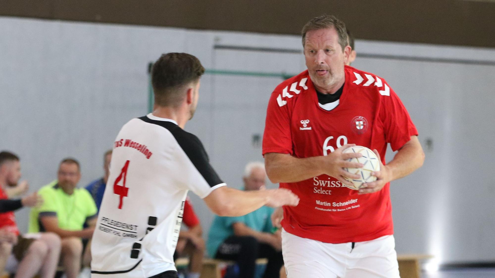 Zülpichs Spielertrainer Olaf Pohlmeier hat den Ball in der Hand, ein Gegner steht ihm gegenüber. Pohlmeier hat die Zunge rausgestreckt.