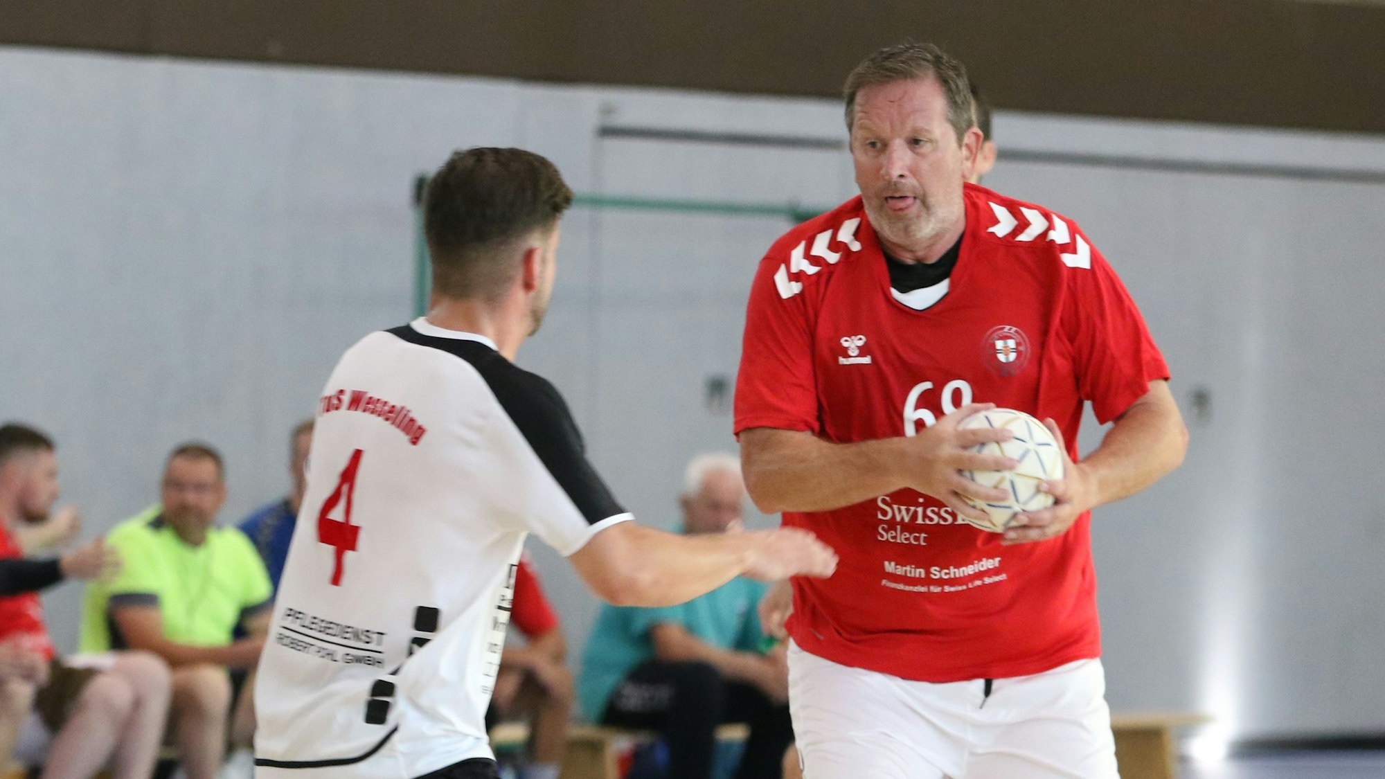 Zülpichs Spielertrainer Olaf Pohlmeier hat den Ball in der Hand, ein Gegner steht ihm gegenüber. Pohlmeier hat die Zunge rausgestreckt.