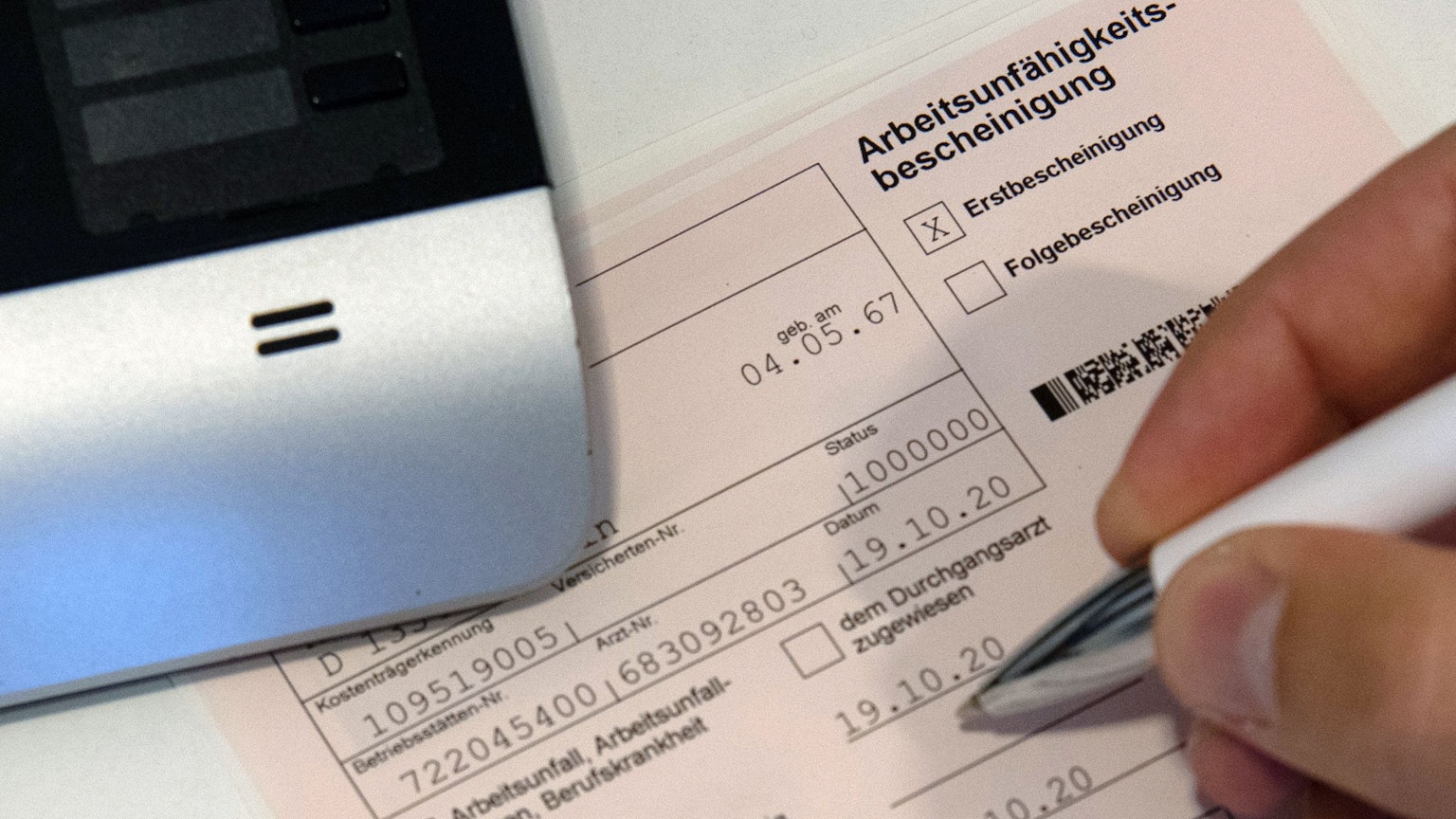 Ein Mitarbeiter einer Arztpraxis notiert etwas auf einer Arbeitsunfähigkeitsbescheinigung (gestellte Szene mit gestellten Daten).