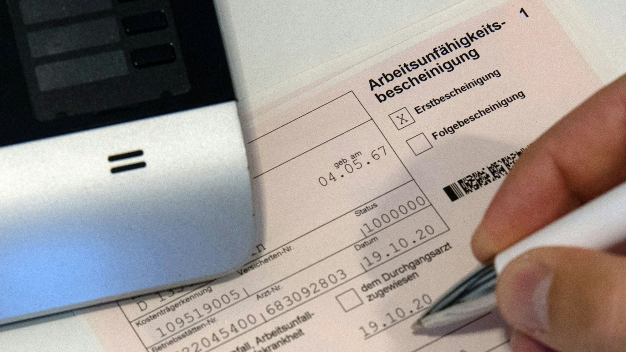 Ein Mitarbeiter einer Arztpraxis notiert etwas auf einer Arbeitsunfähigkeitsbescheinigung (gestellte Szene mit gestellten Daten).