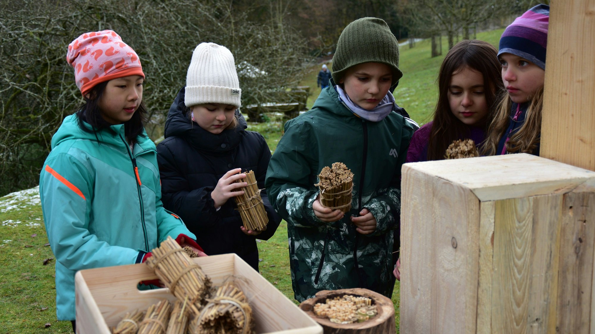 Kinder stehen vor einem Insektenhotel, den sie befüllen.