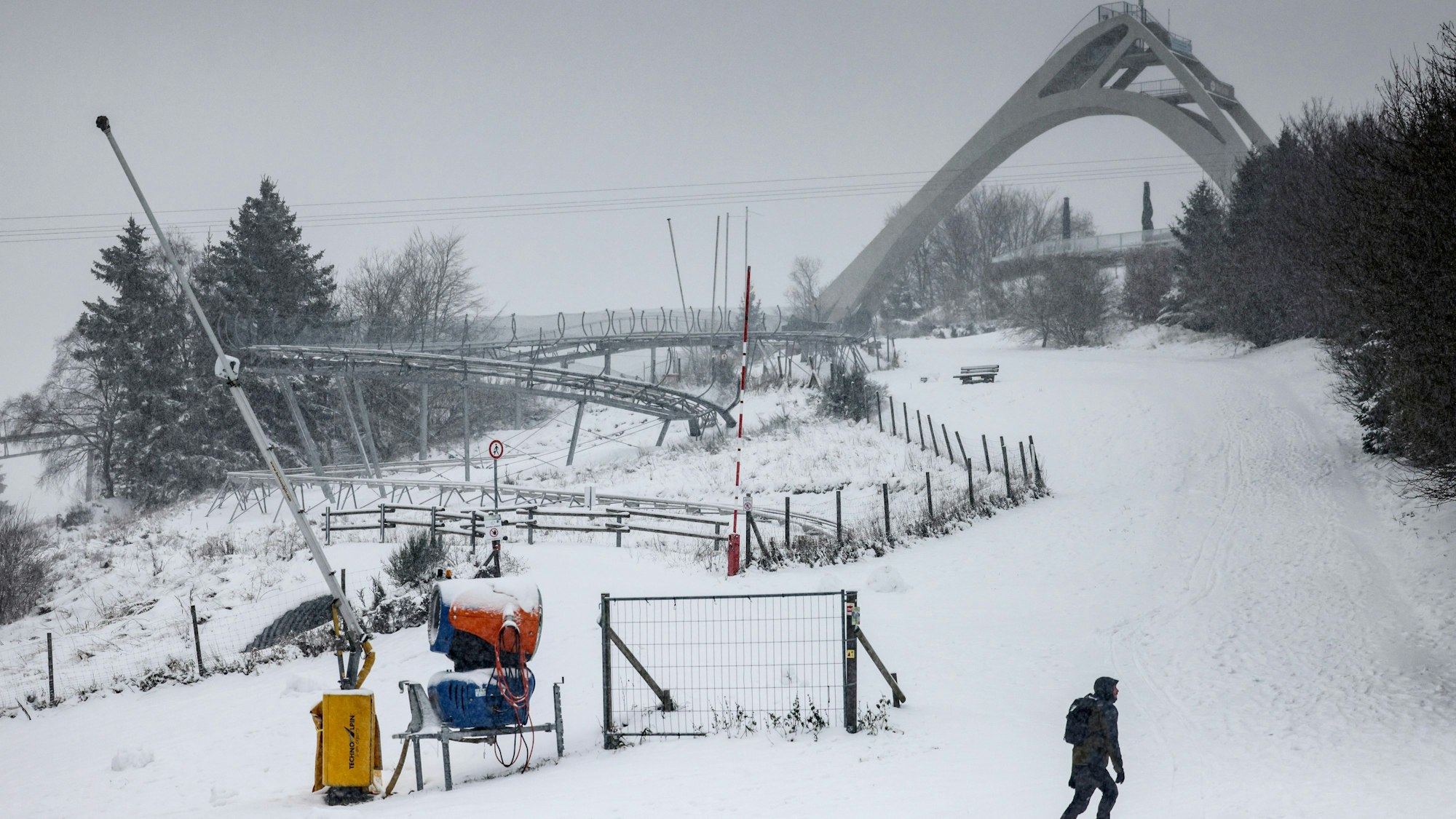 27.11.2023, Nordrhein-Westfalen, Winterberg: Ein Mann spaziert in Winterberg vor der Sprungschanze entlang. Das nasskalte Wetter hält in Nordrhein-Westfalen an. Oberhalb von 300 bis 400 Metern hat es weitere Schneefälle gegeben, in tieferen Lagen Regen oder Schneeregen. (Zu dpa ·Nasskaltes Wetter in NRW hält an - Neuschnee in Höhenlagen·) Foto: Oliver Berg/dpa +++ dpa-Bildfunk +++
